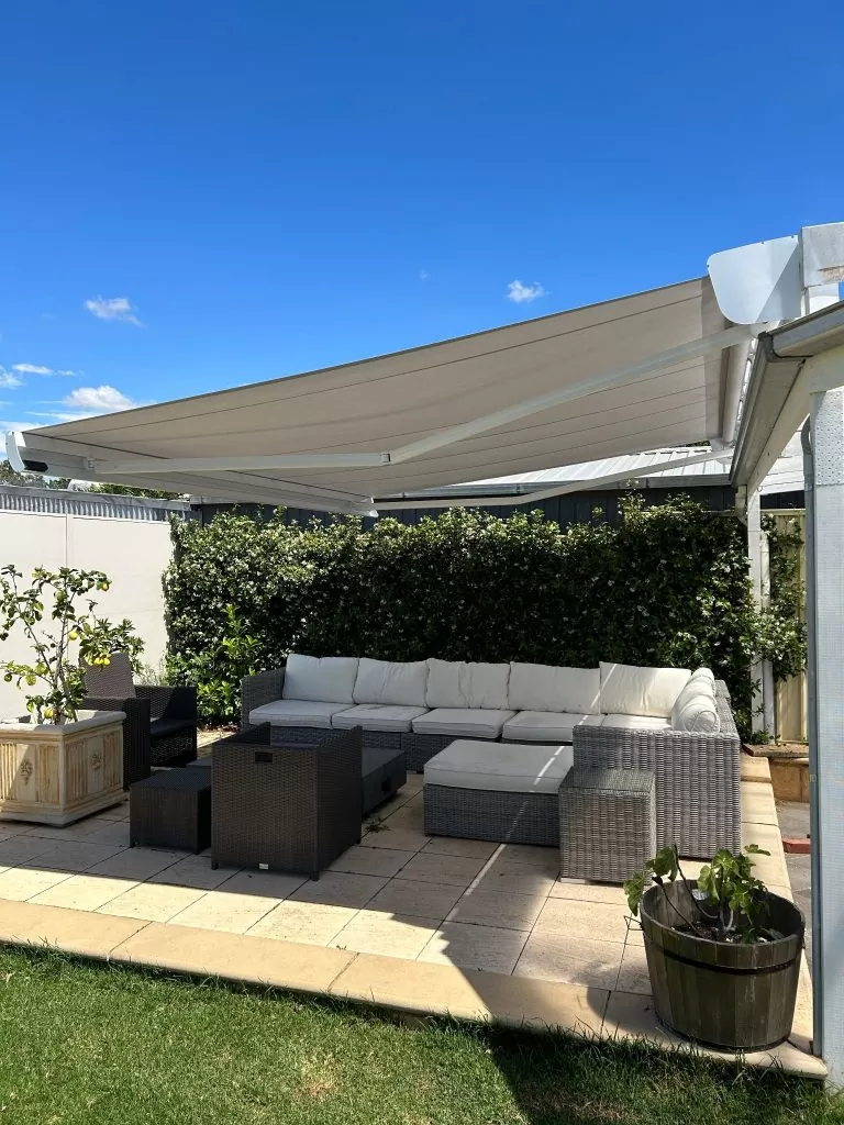 retractable awning fully extended over a paved outdoor entertainment area with a white outdoor lounge and table